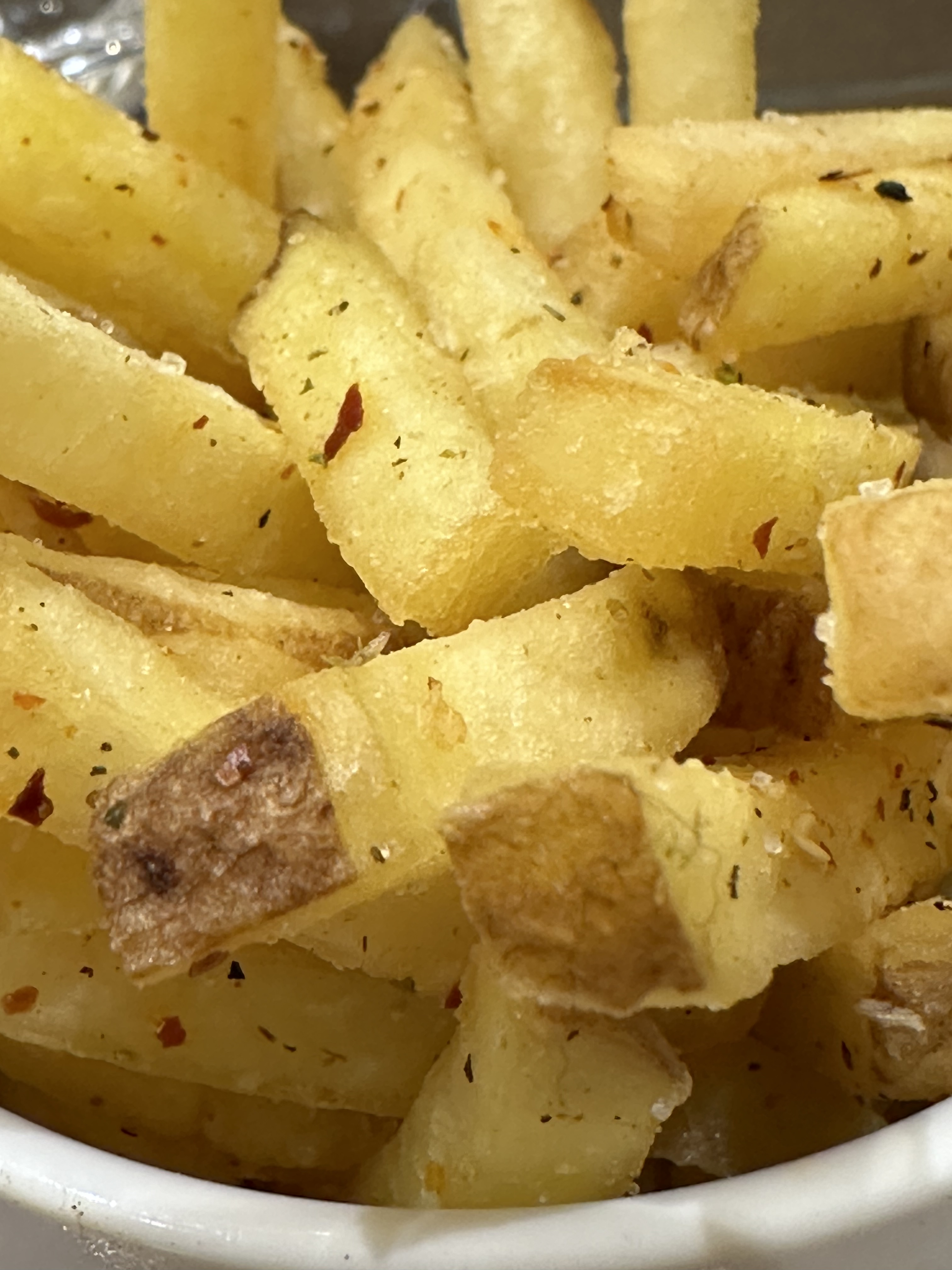 A close-up image of golden, crisp-looking french-fry style chips with a sprinkling of red and black spices.